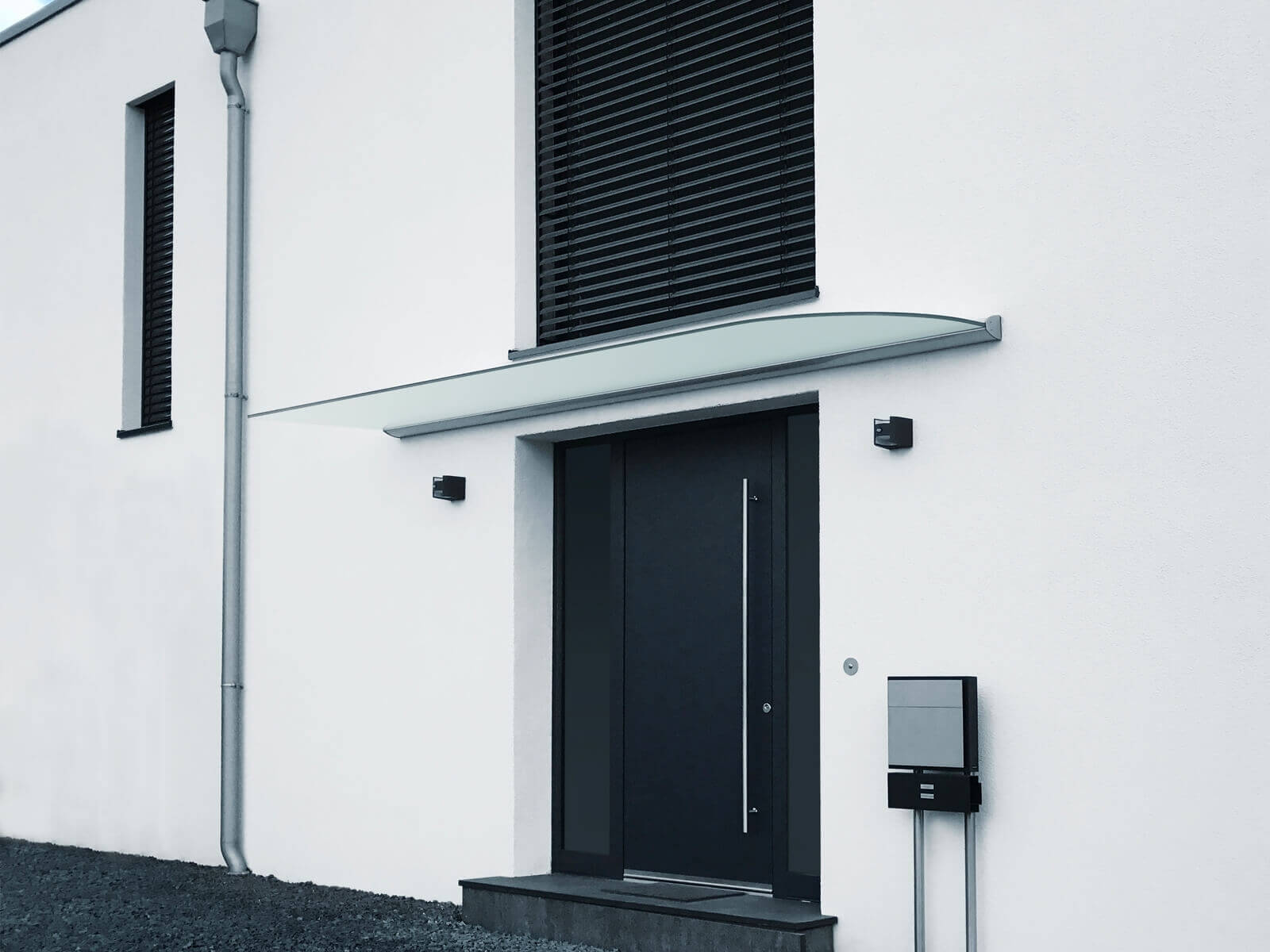 Vordach aus Glas mit Abrundung vor Hauseingang an weißer Fassade